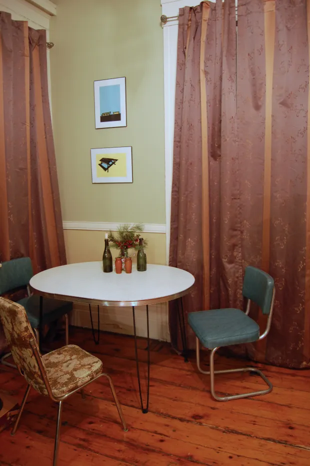 Small dining nook with round white table, teal and floral chairs, patterned curtains, and framed art on a pale green wall